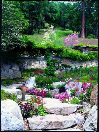 Granite stepping stones weave a path through the courtyard garden with perennial color and native groundcovers. Dogwoods bloom on the hillside beyond.